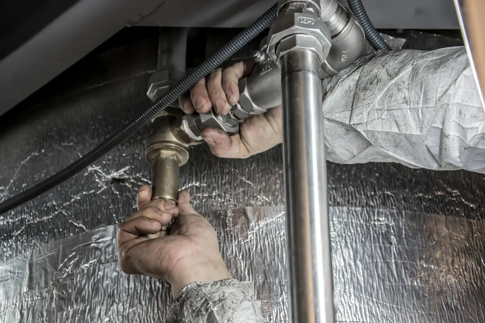 Handen draaien een koppeling vast aan een waterleiding onder een plafond